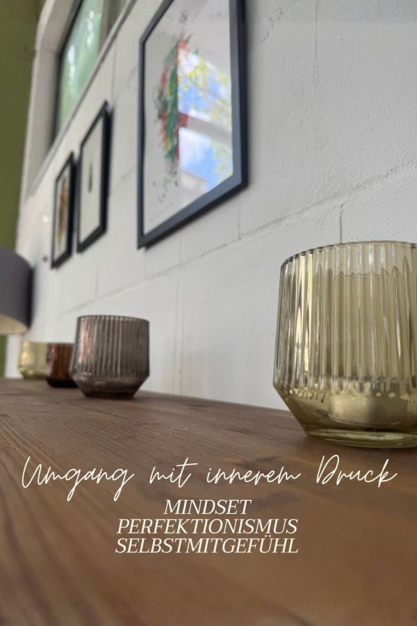 Das Bild zeigt eine mehrere Kerzenhalter auf einem Holzbrett das an einer weißen Wand befestigt ist. Im Hintergrund verschiede unscharfe Bilder.