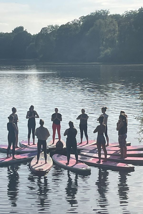 Das Bild zeigt SUB Yoga Teilnehmer auf den Boards im Kreis in der Bergposition stehend im Sonnenschein und auf dem ruhigen See.